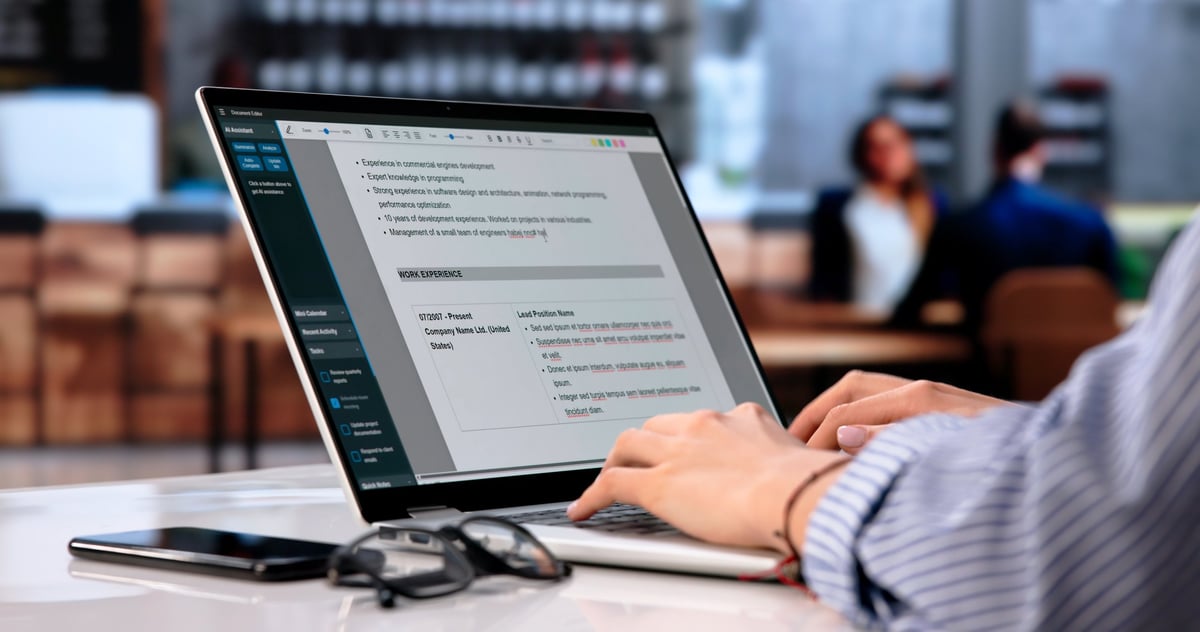 Young Woman Writes Professional Resume On Laptop While Enjoying Coffee Shop Ambiance.
